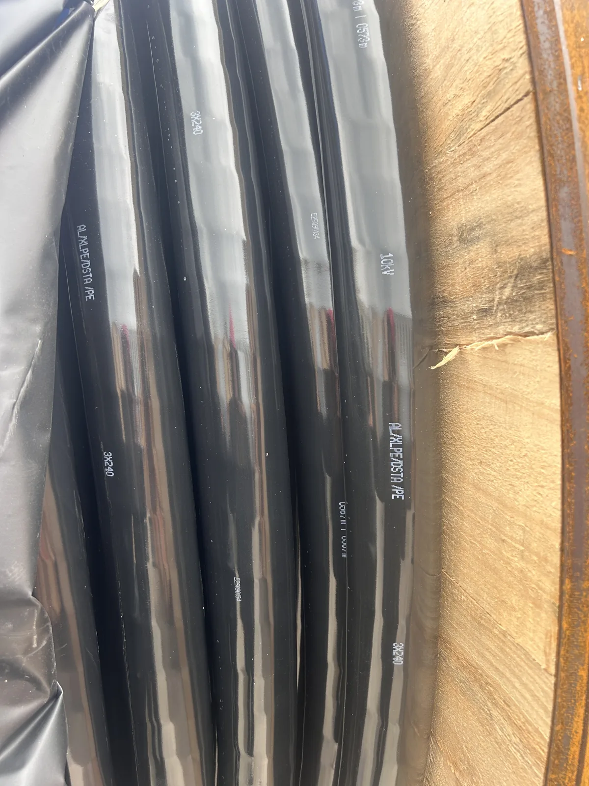 Black outer sheath of a medium-voltage power cable wound on a wooden drum with white printed marking showing construction, core size and voltage