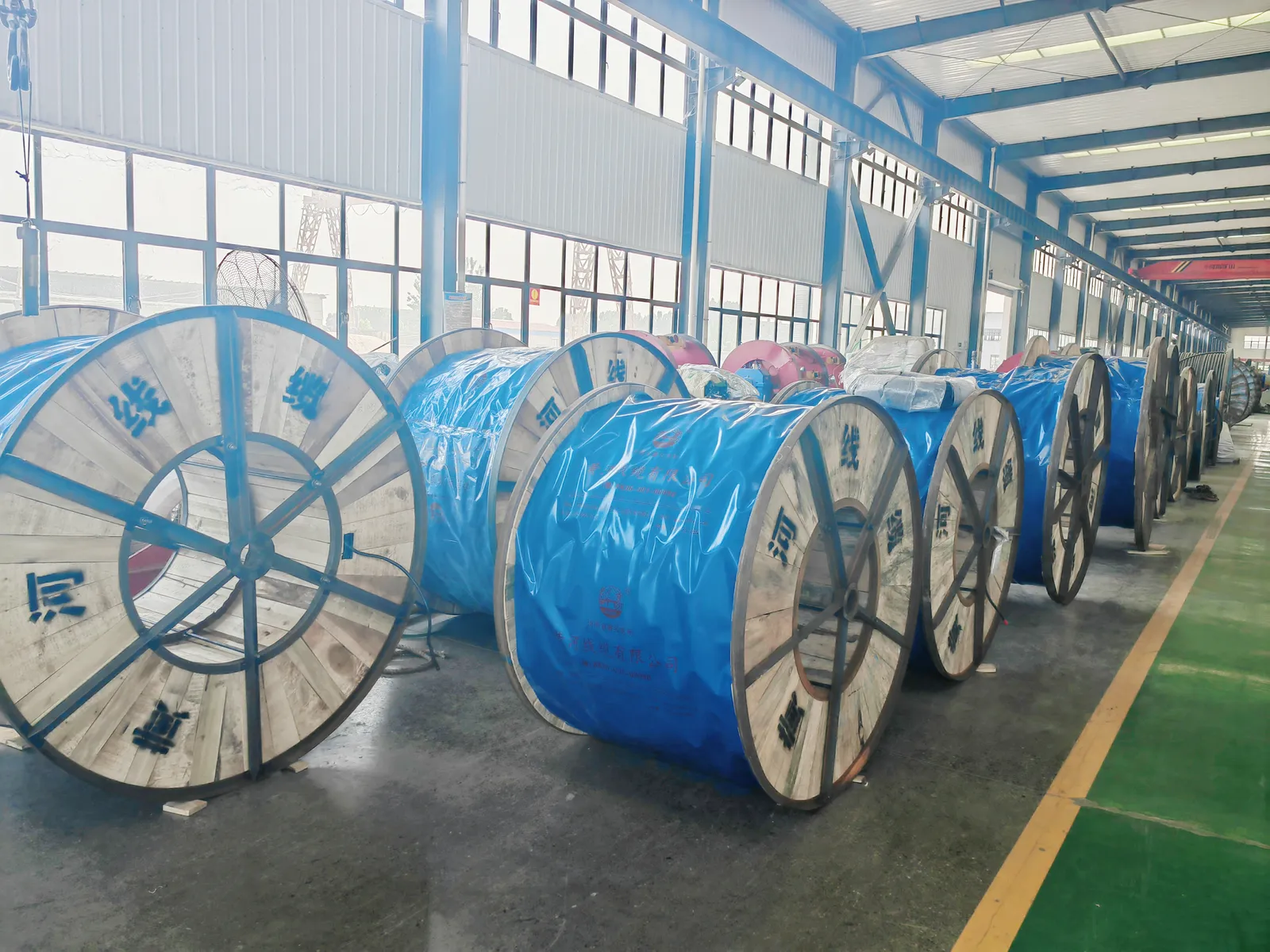 Rows of wooden cable drums with Chinese factory lettering on the flanges, wrapped in blue protective film, in a factory finished-goods warehouse